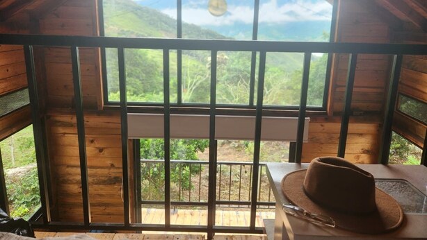Une cabane en bois avec une grande fenêtre, une ampoule suspendue et un chapeau posé sur une table.