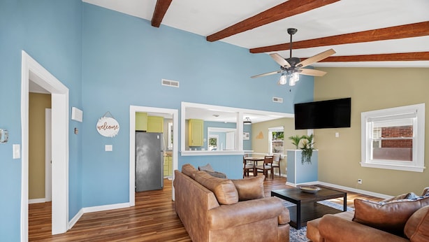 A spacious living area with a wooden floor, a brown leather sofa, a coffee table, and a ceiling fan. - Family Beach House · Sleeps 6 · 2 Blks · 6 Parking (Virginia Beach)