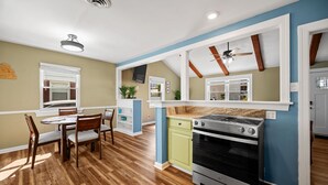 A kitchen with wooden flooring, a built-in oven, and a dining area with chairs and a table. - Family Beach House · Sleeps 6 · 2 Blks · 6 Parking (Virginia Beach)