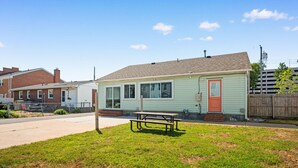 A single-story building with a front door, windows, and a picnic table in the yard. - Family Beach House · Sleeps 6 · 2 Blks · 6 Parking (Virginia Beach)