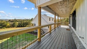 Une terrasse en bois avec une balustrade, un porche couvert et une vue sur une maison blanche et le paysage environnant.