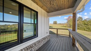 Ein überdachter Balkon mit Blick auf ein Wiesfeld und Bäume.
