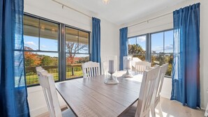 Uma área de refeições com mesa de madeira, cadeiras brancas e cortinas azuis.