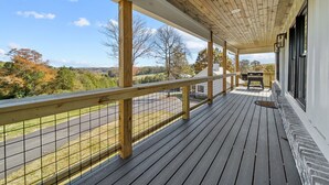 Um deck de madeira com guarda-corpo, uma churrasqueira e vista para a estrada e árvores.