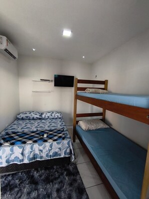 A room with a bunk bed, a flat bed with patterned bedding, a mounted television, and an air conditioning unit.