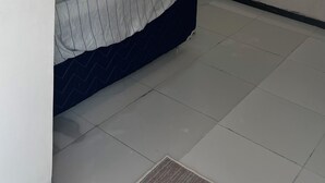 Ein Schlafzimmer mit einem Bett, einem Fernseher auf einem Standfuß, einer Klimaanlage an der Wand und einem Fliesenboden.