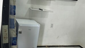 Ein kompakter Raum mit einem weißen Kühlschrank, einem an der Wand montierten Flachbildfernseher und einem Bett mit einer Karo-Decke.
