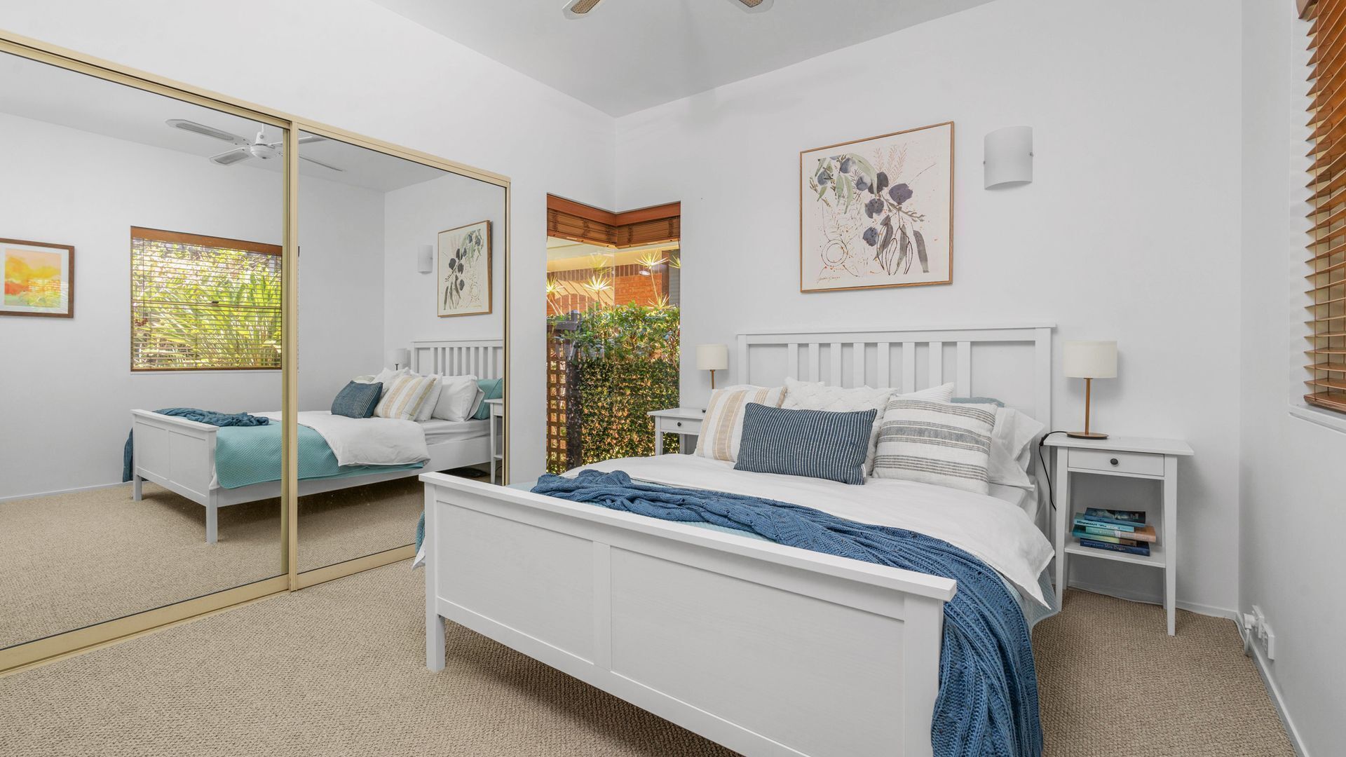 A bedroom with a white bed, a bedside table with a lamp, a mirror, and artwork on the wall.