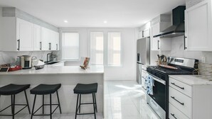 Een moderne keuken met witte kasten, een centraal eiland met krukken, een fornuis en een ingebouwde oven.