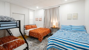 Een kamer met stapelbedden, een enkel bed, een nachtkastje met een lamp en een raam met gordijnen.