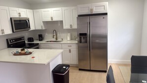 A modern kitchen with white cabinets, a stainless steel refrigerator, a microwave, and a coffee maker. - Charming 2BR/2BA Getaway – Feels Like Home (Tampa)