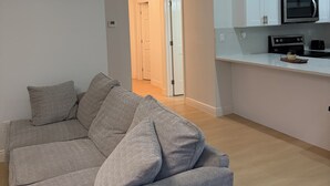 A modern living room with a grey sectional sofa, a kitchen with white cabinets and appliances, and a hallway leading to another room. - Charming 2BR/2BA Getaway – Feels Like Home (Tampa)