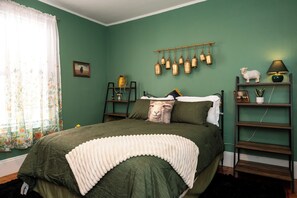 A bedroom with a bed, a shelf with decorative items, and a wall-mounted light fixture.