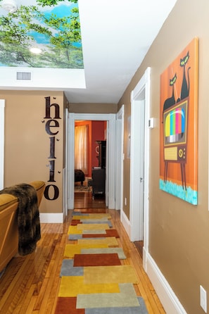 A hallway with a colorful rug, a painting of cats, and a ceiling mural.