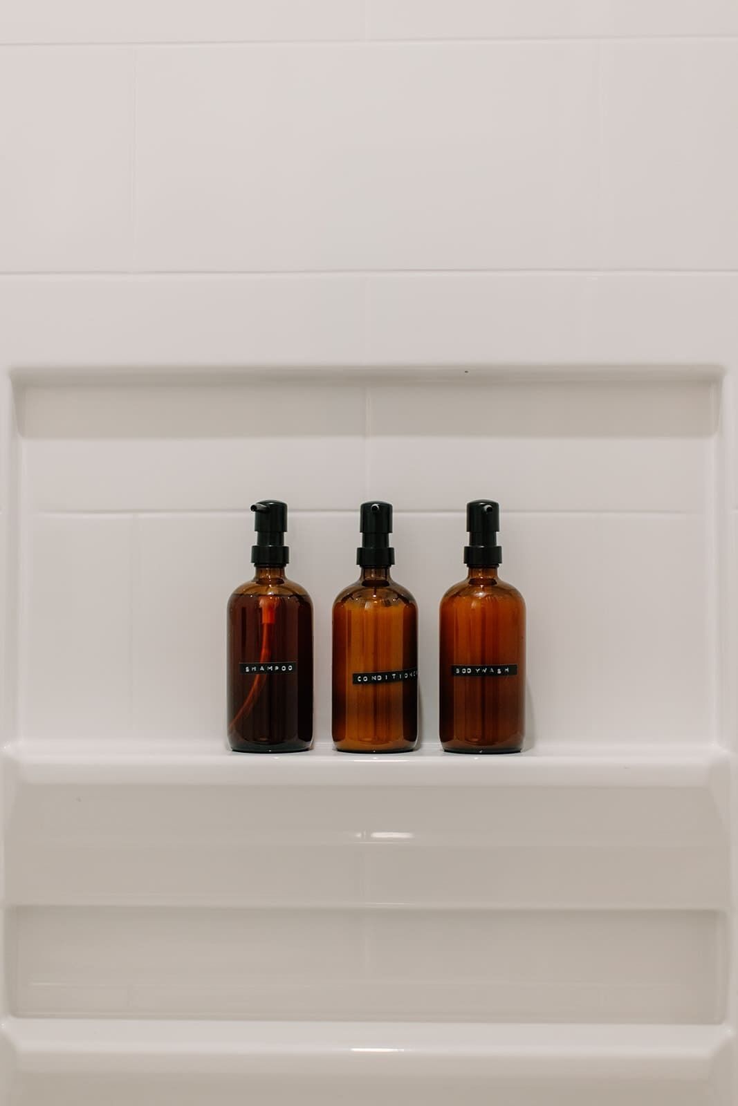 Three amber bottles with black caps on a white shelf.