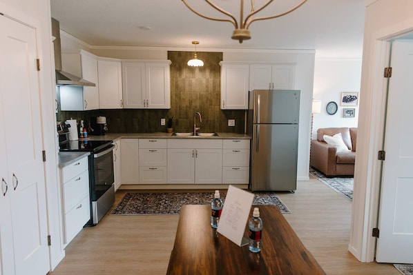 A modern kitchen with white cabinets, a stainless steel refrigerator, and a wooden dining table.