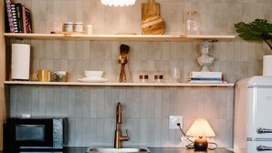 A kitchen with blue cabinets, a microwave, a sink, and a hanging light fixture.