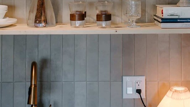A kitchen with a wooden cutting board, glass jars, a brush, and a sculpture on shelves.