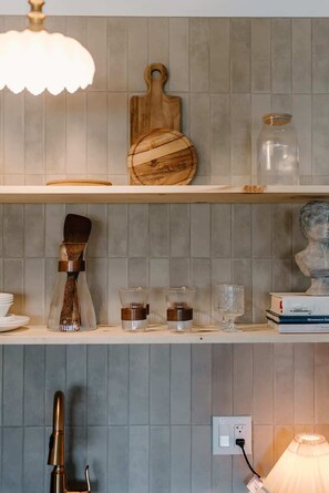 Une cuisine avec une planche à découper en bois, des bocaux en verre, un pinceau et une sculpture posée sur des étagères.