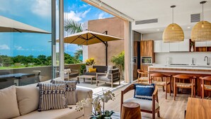 Uma sala de estar moderna e integrada, com sofá, mesa de jantar e cadeiras, cozinha com ilha grande e varanda com mobiliário para área externa.