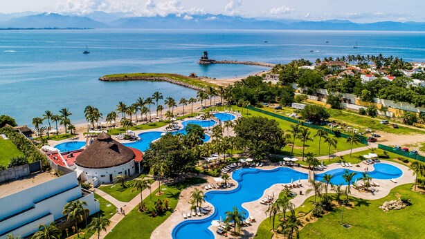 Resort com várias piscinas, palmeiras e vista para o oceano.