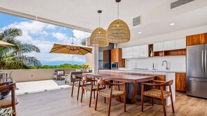 Cozinha moderna com ilha de madeira, luminárias pendentes e vista para o oceano.