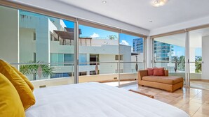 A modern hotel room with a large bed, a sofa, and a balcony with a view of other buildings. - Spacious Penthouse with ocean views, pool & balcony (Nuevo Vallarta)