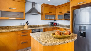 A kitchen with wooden cabinets, granite countertops, a stainless steel refrigerator, and a microwave. - Spacious Penthouse with ocean views, pool & balcony (Nuevo Vallarta)