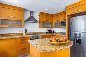 A kitchen with wooden cabinets, granite countertops, a stainless steel refrigerator, and a microwave. - Spacious Penthouse with ocean views, pool & balcony (Nuevo Vallarta)