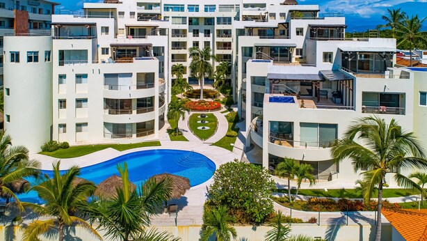 A modern hotel with multiple floors, a central courtyard with a swimming pool, and surrounding greenery. - Spacious Penthouse with ocean views, pool & balcony (Nuevo Vallarta)