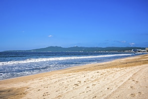Uma praia com céu limpo, ondas e montanhas ao longe.