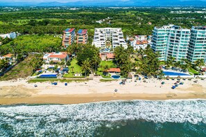 Eine Luftaufnahme eines Küstenresorts mit Strandvillen, einem Pool und einer Strandfläche.