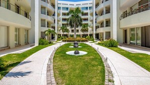 Un edificio moderno de varios pisos con un patio central, palmeras y una fuente.