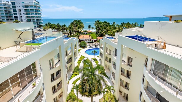 Un hotel de varios pisos con piscina en la azotea, palmeras y vistas al océano.