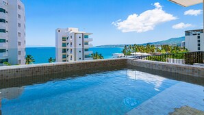 A swimming pool with a view of the sea, surrounded by modern buildings. - Modern condo with infinity pool, WiFI, plunge spa & ocean-view balcony (Nuevo Vallarta)