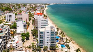 A coastal cityscape with high-rise buildings, a beach, and a clear view of the ocean. - Modern condo with infinity pool, WiFI, plunge spa & ocean-view balcony (Nuevo Vallarta)