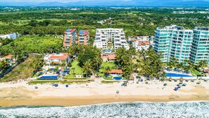 A coastal hotel with multiple buildings, a beach, and palm trees. - Luxurious Penthouse with a scenic terrace pool & modern kitchen (Nuevo Vallarta)