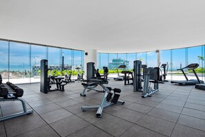 Une salle de sport équipée de divers appareils d’exercice, dotée de grandes fenêtres et offrant une vue sur des bâtiments et des espaces verts.