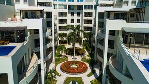 Un hôtel à plusieurs étages doté de balcons, d’une cour intérieure avec un parterre floral circulaire et d’une piscine.
