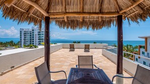 A covered outdoor seating area with a view of the ocean and buildings in the background. - Bright coastal apartment with pool, balcony & beach access close by (Nuevo Vallarta)