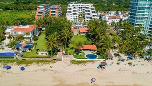 An aerial view of a resort with multiple buildings, a beach, and palm trees. - Bright coastal apartment with pool, balcony & beach access close by (Nuevo Vallarta)