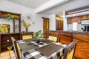 A dining area with a checkered tablecloth, wooden chairs, a potted plant, and a decorative wall piece. - Puerto de Luna #622 | 1BR/2BA Puerto Vallarta | Pool, beach & dining (Puerto Vallarta)