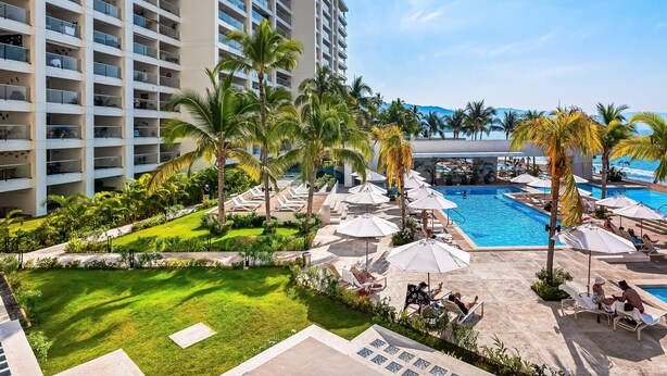 Un hôtel doté d’une piscine, de palmiers et de chaises longues.