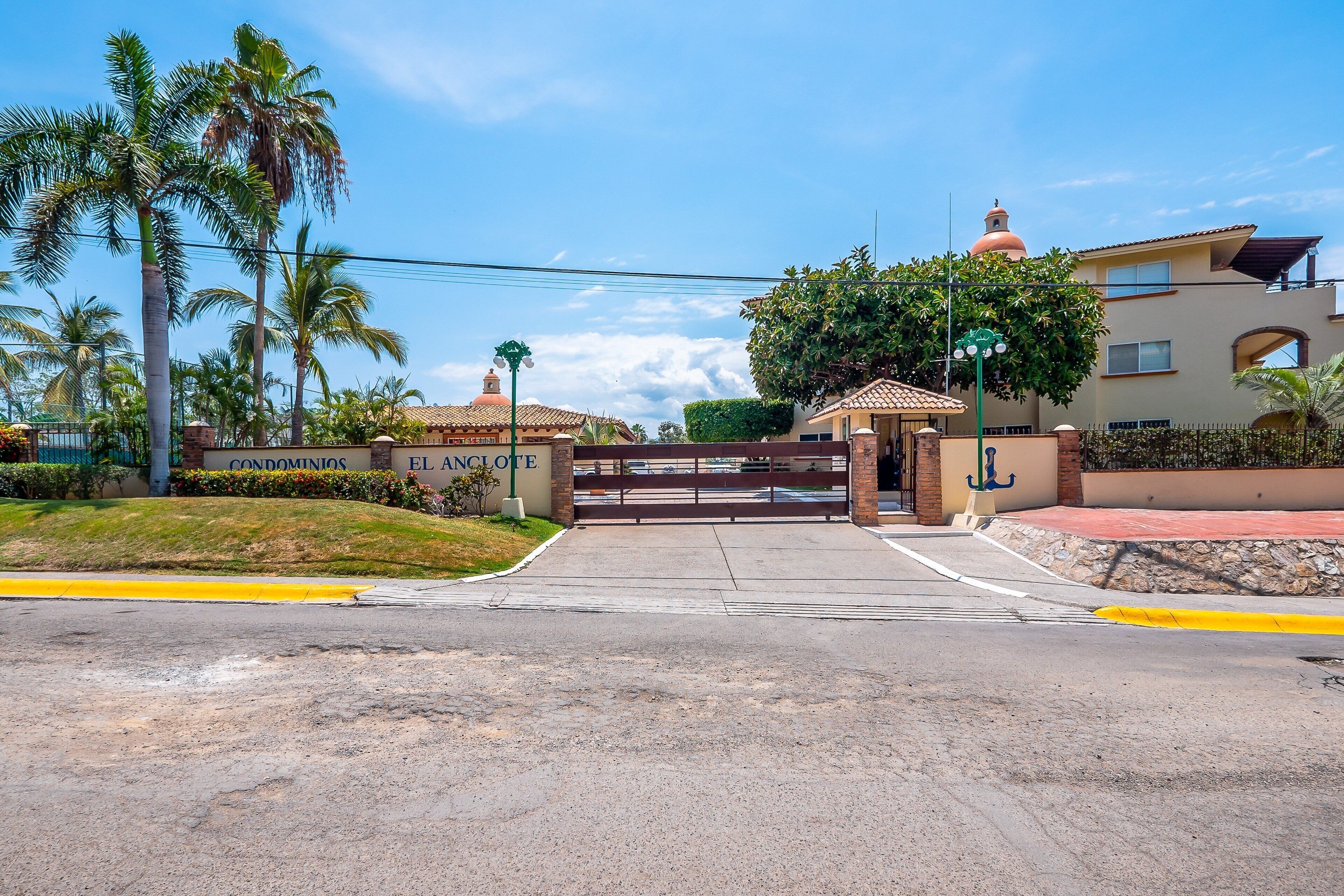 A gated entrance to a residential area with a sign reading 'CONDOMINIOS EL ANCLOTE.'
