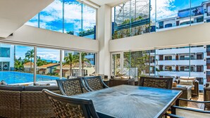 A spacious indoor area with a large table and chairs, large windows offering views of a pool and buildings, and a balcony with outdoor seating. - Viva la vida Life 309 | 1BR/2BA Bucerias, near ocean, pool, balcony, WiFi (Bahia de Banderas)