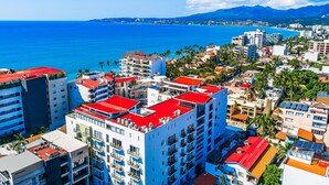 A coastal cityscape with high-rise buildings, a clear blue sea, and a mountainous backdrop. - Viva la vida Life 309 | 1BR/2BA Bucerias, near ocean, pool, balcony, WiFi (Bahia de Banderas)