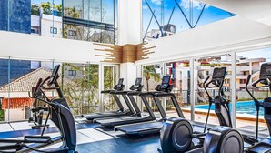 A gym with treadmills, stationary bikes, and a pool visible through large windows. - Viva la vida Life 309 | 1BR/2BA Bucerias, near ocean, pool, balcony, WiFi (Bahia de Banderas)