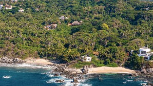 Eine Küstenlandschaft mit Häusern, die von dichter Vegetation und einem Strand umgeben sind.