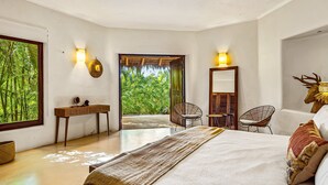 Ein Schlafzimmer mit Bett, Schreibtisch, zwei Stühlen, einem Spiegel und Blick auf Grünflächen.