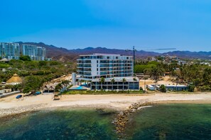 Ein mehrstöckiges Hotel mit Pool, Zugang zum Strand und einem Bergpanorama im Hintergrund.
